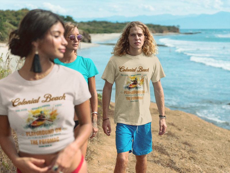 Group of friends walking along a scenic coastal path with two wearing Colonial Beach Premium T-Shirts (man in soft cream; woman in soft pink) Playground on the Potomac, ocean waves and cliffs in the background