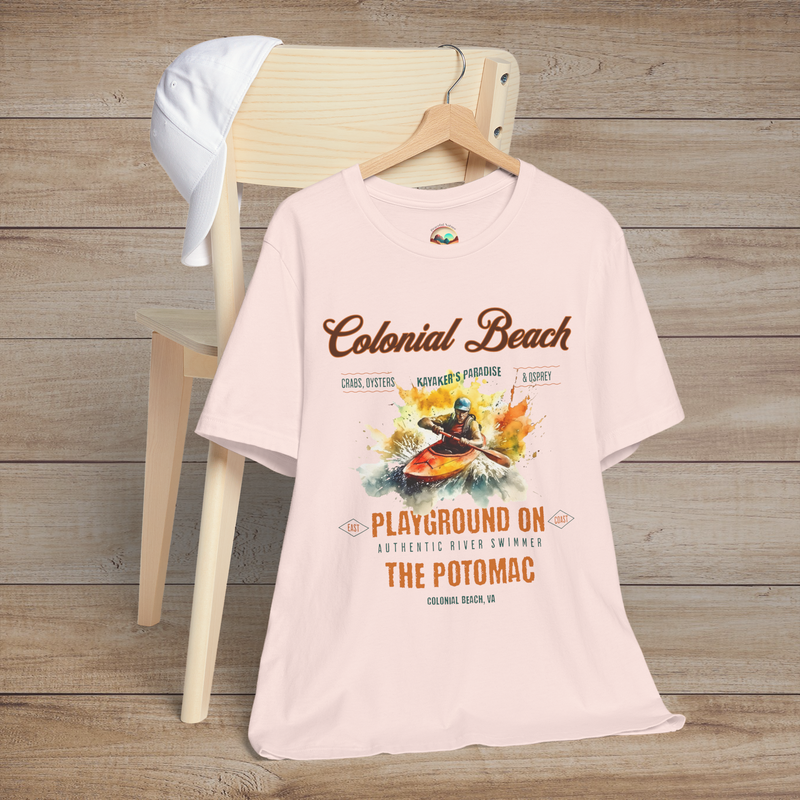 Colonial Beach Premium T-Shirt Playground on the Potomac design showcased on a soft pink t-shirt, placed on a wooden chair next to a white cap, ideal for beach lovers