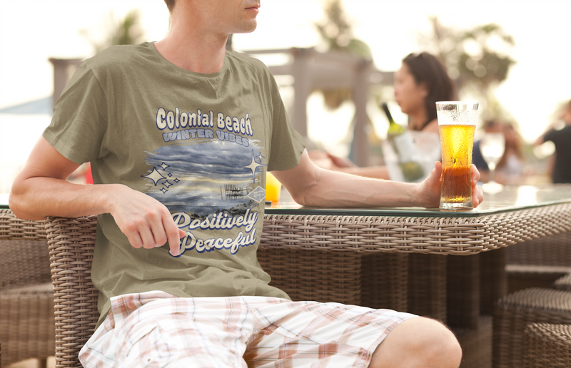 man wearing colonial beach winter vibes heather olive premium t-shirt relaxing at outdoor cafe