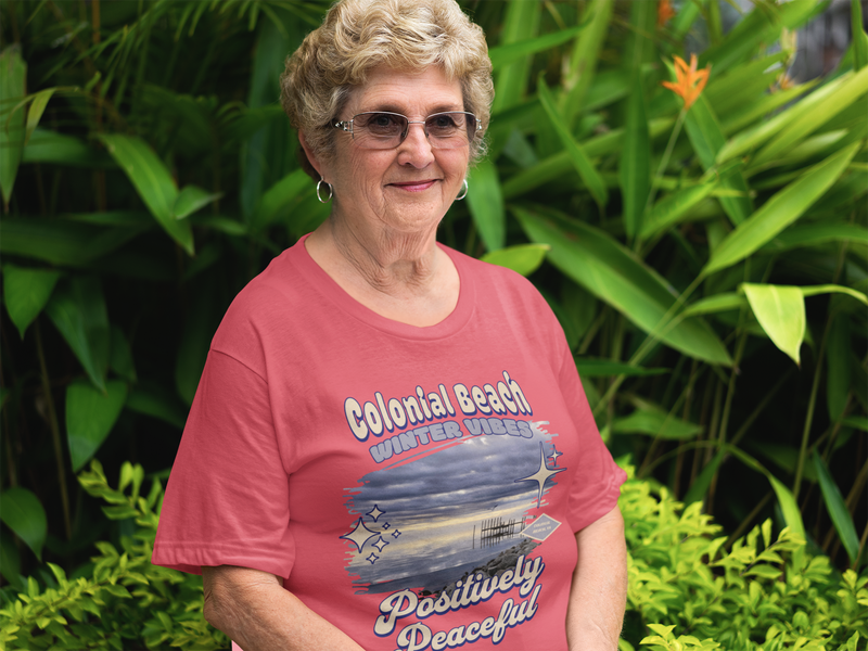 older woman smiling and wearing colonial beach winter vibes heather red premium t-shirt in garden