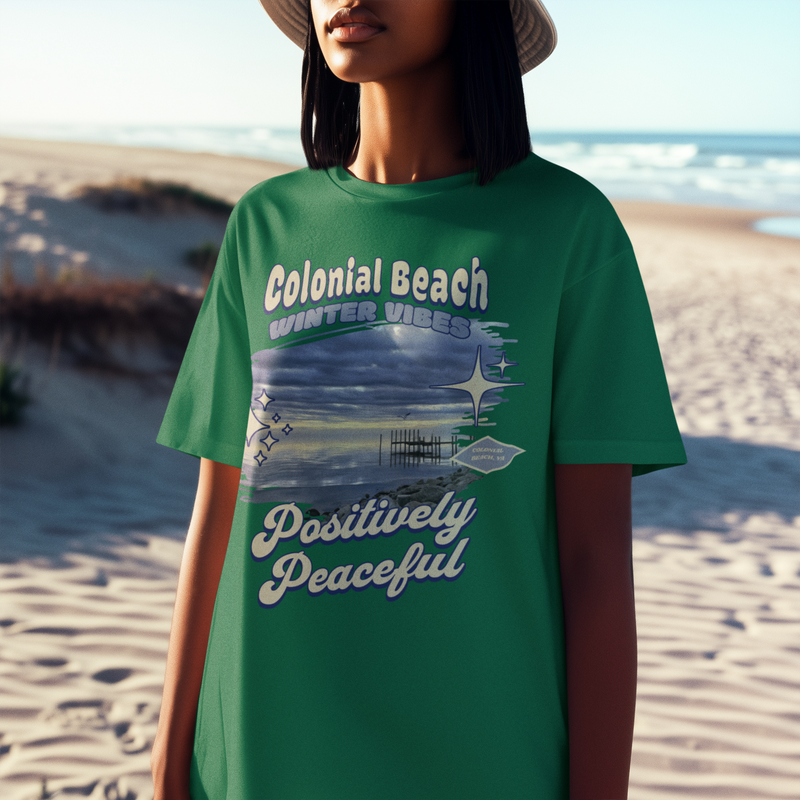 Woman wearing colonial beach winter vibes kelly green premium t-shirt sitting on rocks by the ocean