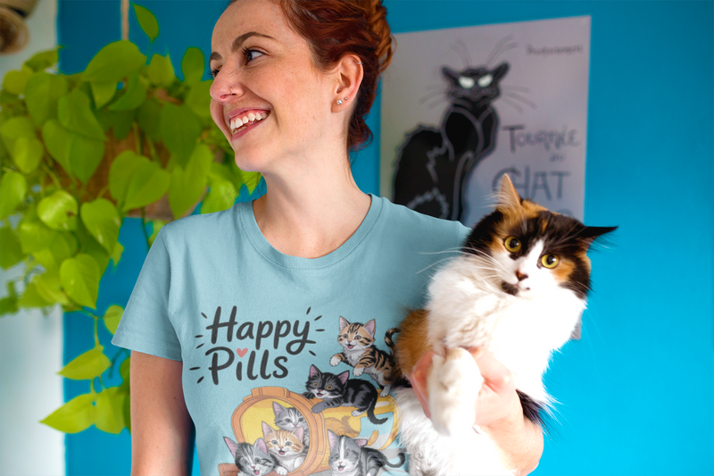 Woman smiling brightly in a turquoise Happy Pills t-shirt while holding a wide-eyed fluffy cat in a vibrant room