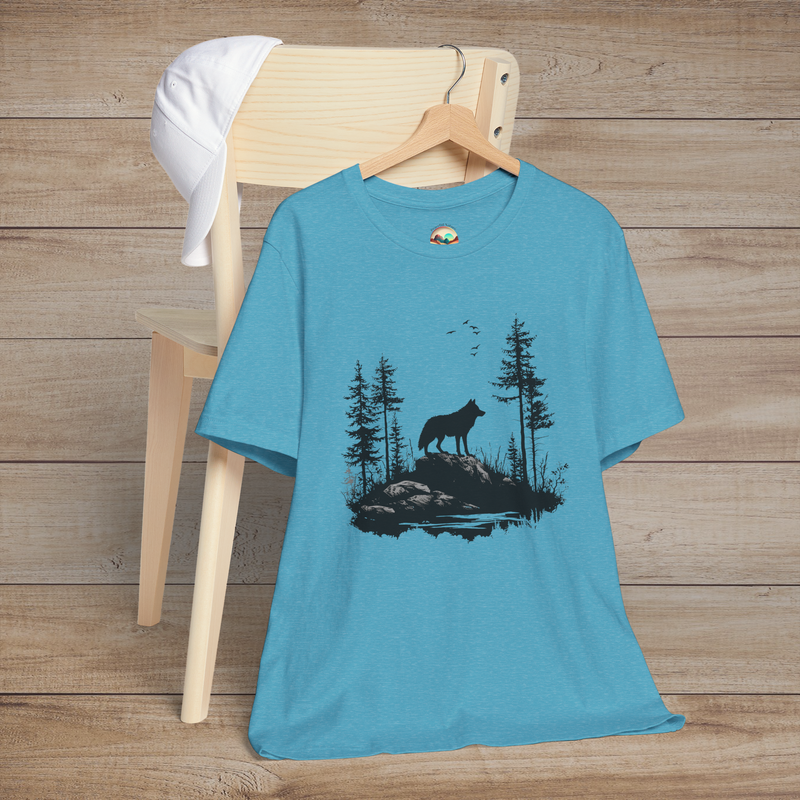 Heather aqua t-shirt displaying a powerful lone wolf standing on a rocky terrain surrounded by pine trees and soaring birds, celebrating resilience