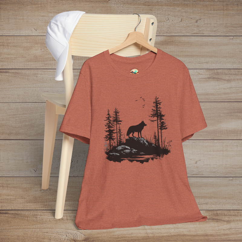 Heather clay t-shirt with a striking black silhouette of a lone wolf among evergreen trees and flying birds, symbolizing harmony with nature