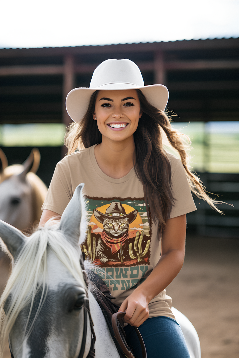Joyful female model riding a horse in the Heather Tan Meowdy Partner Cowboy Cat T-Shirt, Western cat graphic tee