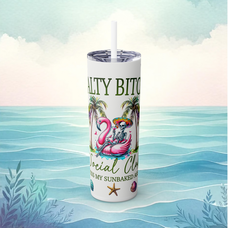 Front view of the Salty Bitch Social Club skinny tumbler in white, with a skeleton floating in a flamingo pool float among palm trees and starfish