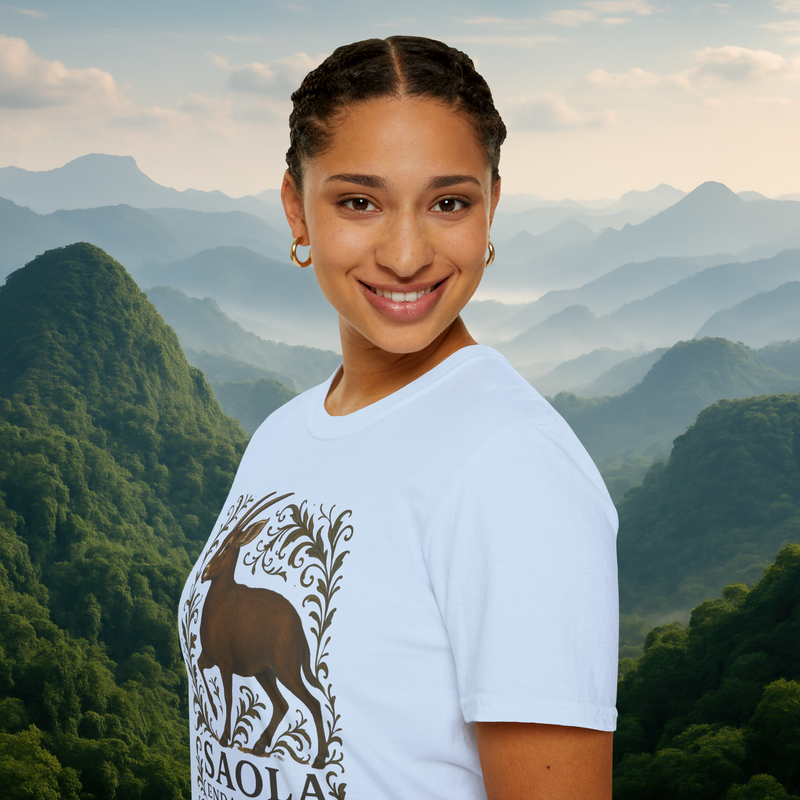 Smiling woman wearing the Saola Endangered Asian Unicorn T-Shirt in Light Blue – featuring a detailed Saola and botanical design, standing before misty green mountains