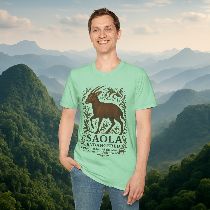 Smiling man wearing the Saola Endangered Asian Unicorn T-Shirt in Mint Green – lightweight soft-style cotton shirt with endangered Saola and botanical design, set against misty green mountains