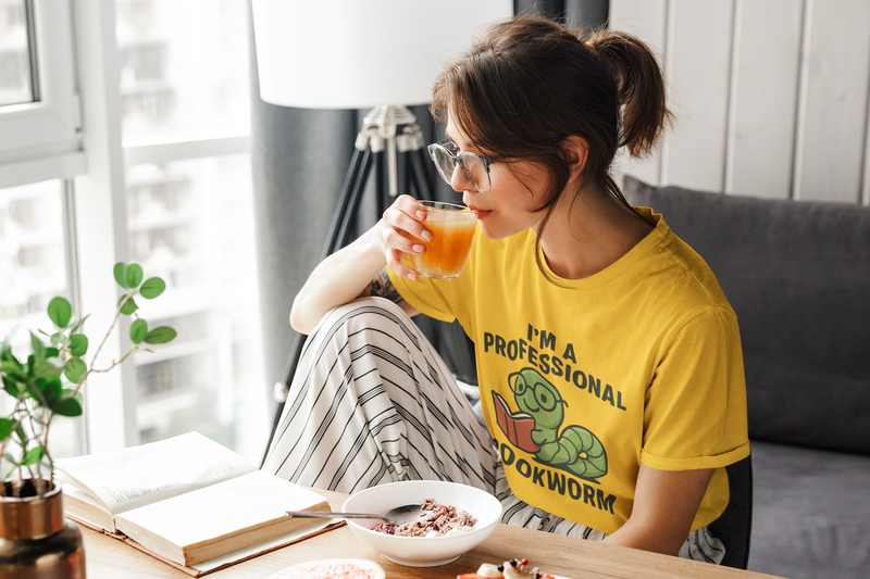 Woman in yellow shirt with a dinosaur graphic sitting on a couch, drinking juice and eating.
