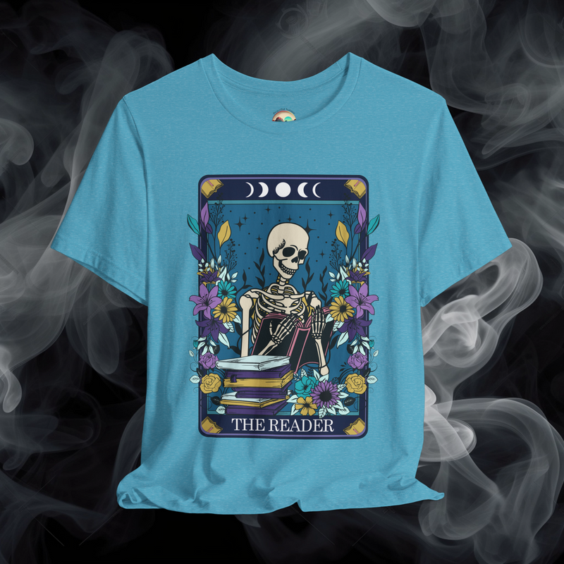 The Reader T-Shirt featuring a mystical skeleton reader in a tarot card frame with flowers and moons, displayed on heather aqua fabric