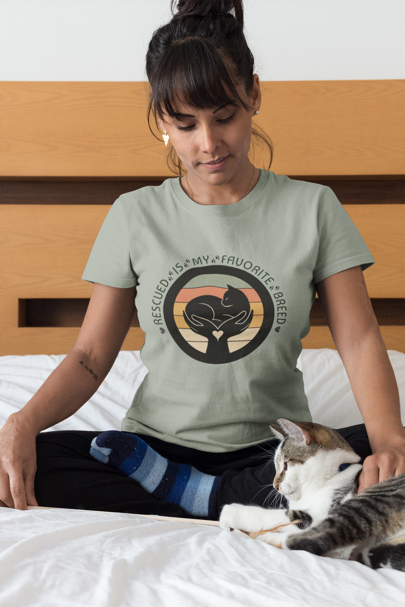 Woman wearing a t-shirt with a cat graphic and text, sitting on a bed with a cat.