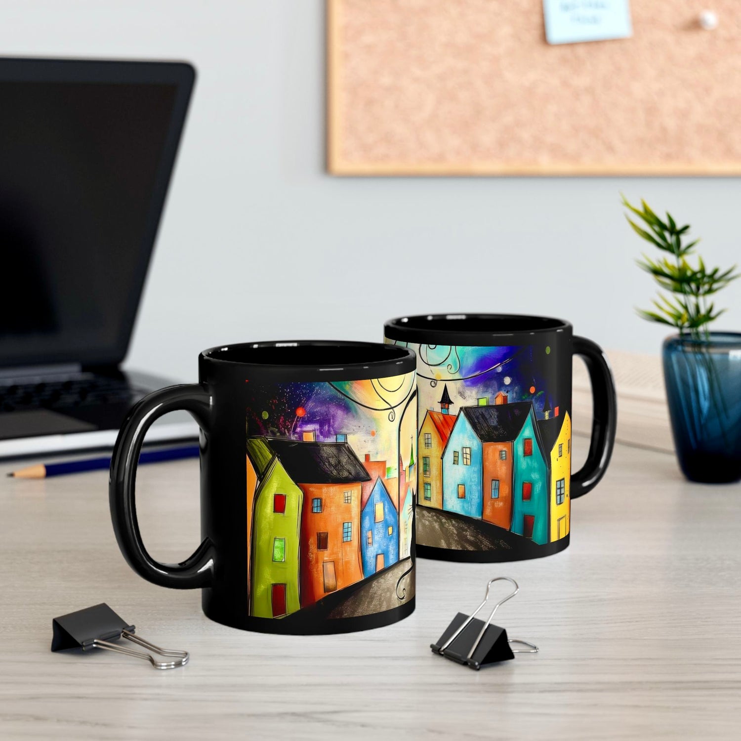 Two black ceramic mugs featuring whimsical black cat and vibrant cityscape artwork, side-by-side on desk