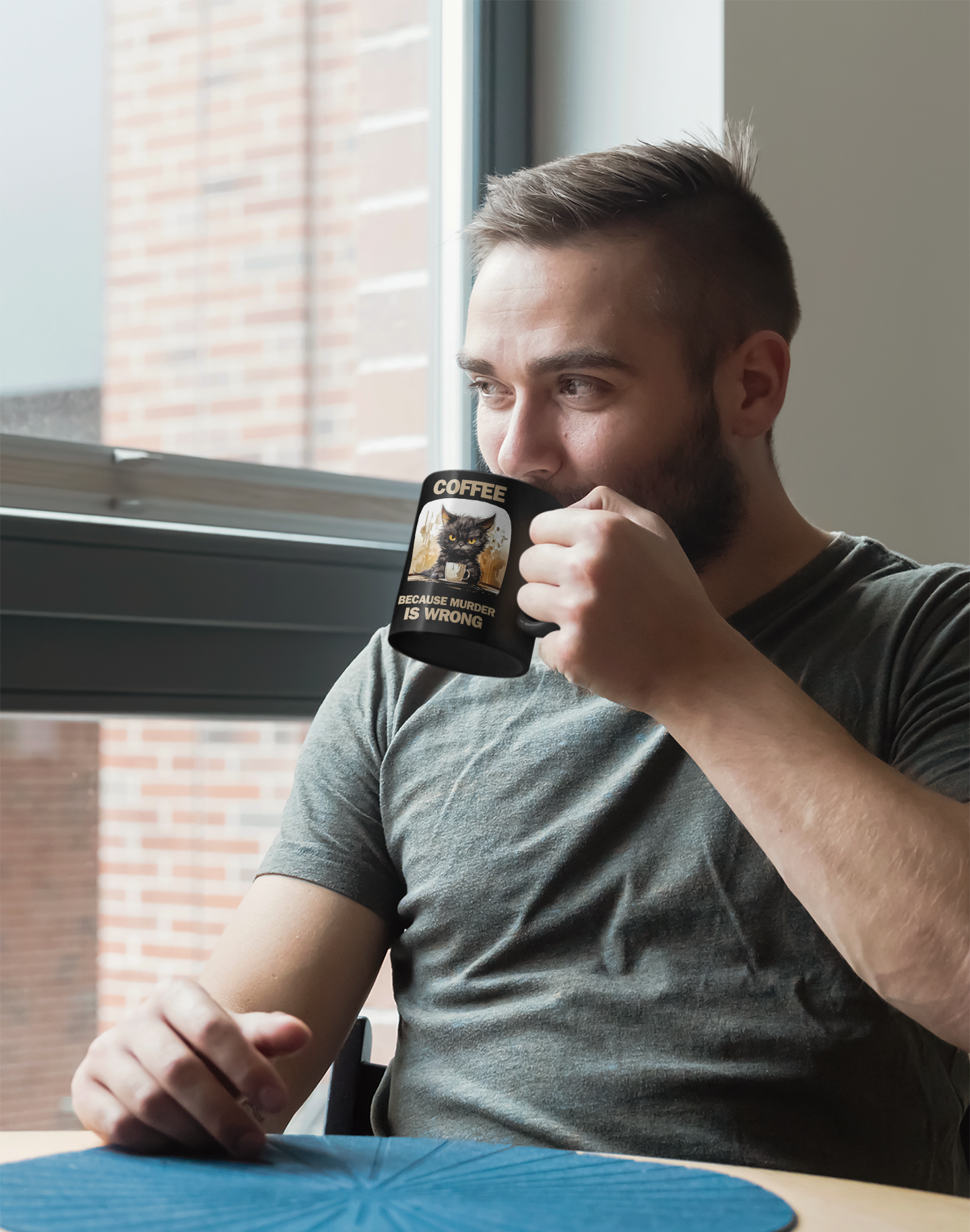 Man sipping coffee from 11 oz black mug, right side view, with angry cat design and funny "Coffee Because Murder Is Wrong" saying