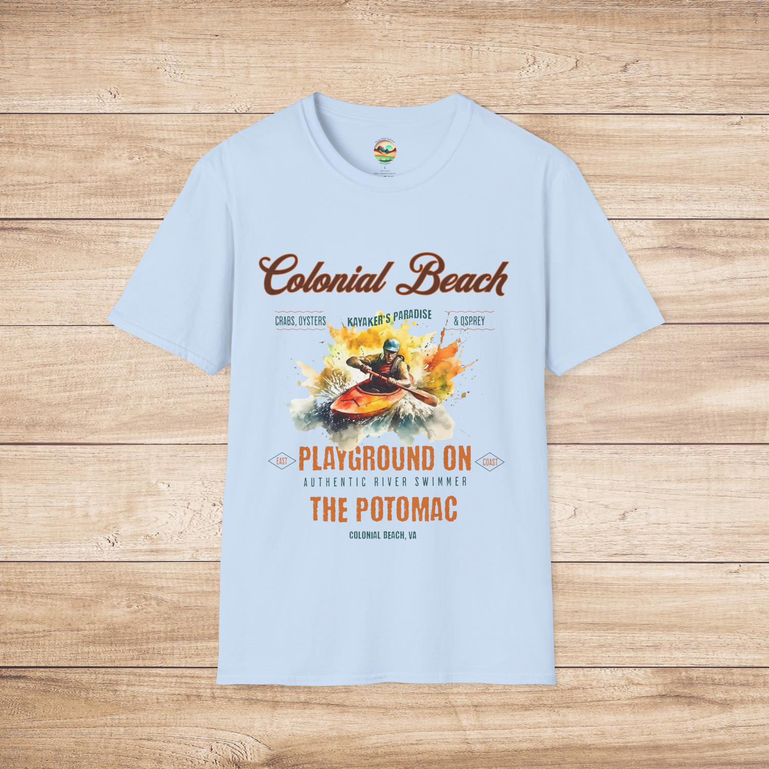 Colonial Beach Soft Fit T-Shirt in Light Blue displayed flat on a rustic wooden background, showcasing a colorful kayaking adventure scene on the Potomac River
