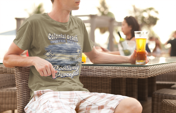 man wearing colonial beach winter vibes heather olive premium t-shirt relaxing at outdoor cafe