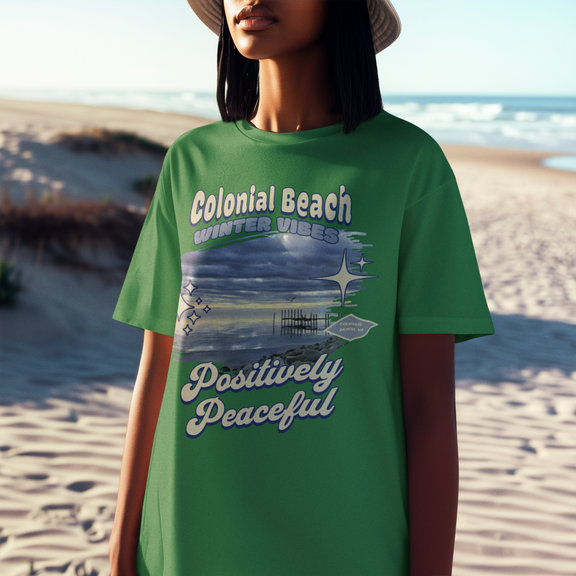 Woman wearing Colonial Beach Winter Vibes turf green t-shirt standing on sandy beach