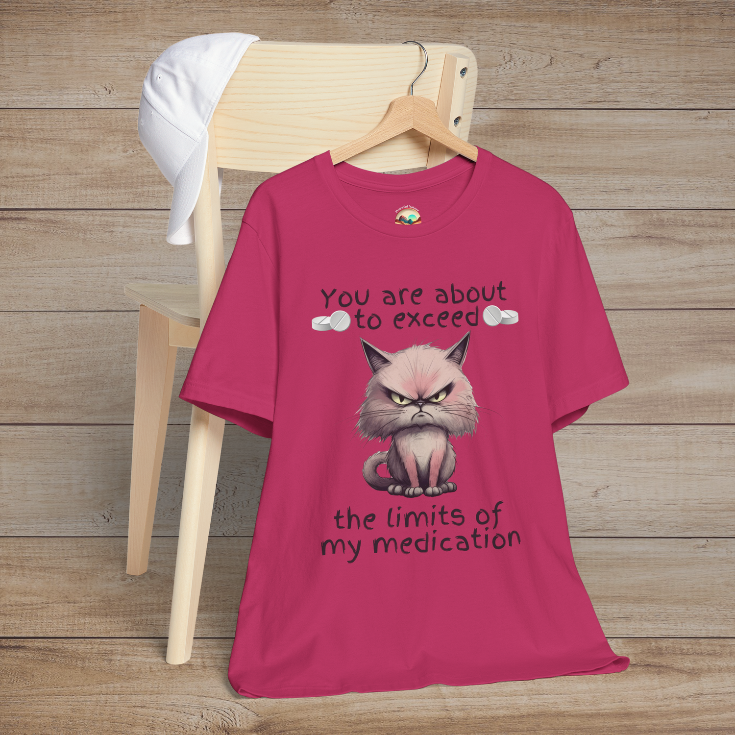 Sarcastic cranky cat t-shirt in berry pink, showing angry cartoon cat and humorous text about testing patience, laid flat on a wooden chair