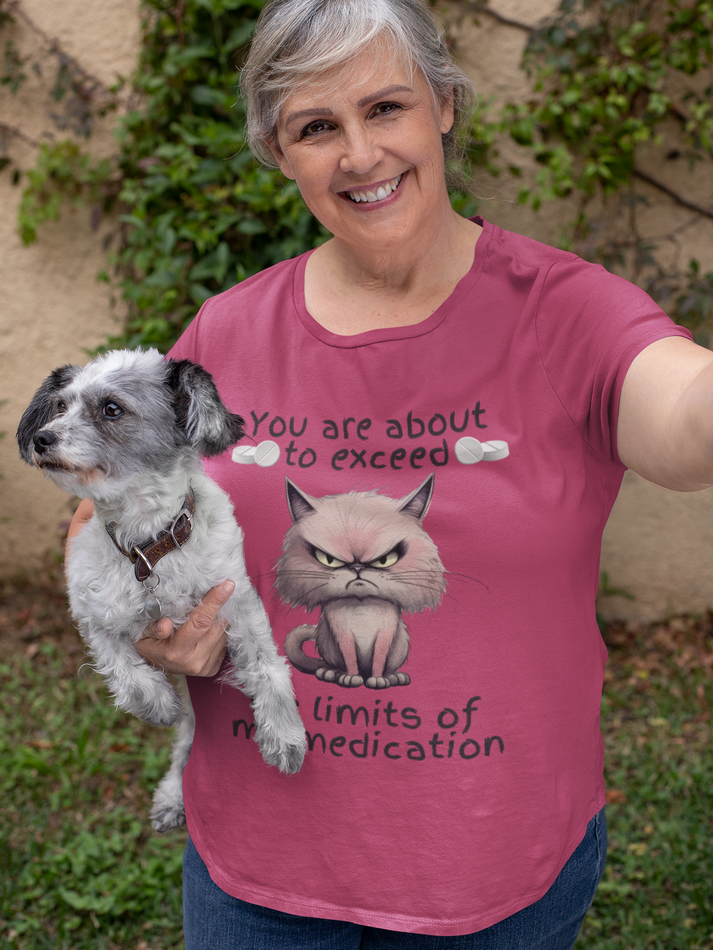 Smiling older woman wearing funny berry pink cranky cat t-shirt with angry cat graphic, posing with dog, perfect gift idea for sarcastic cat lovers