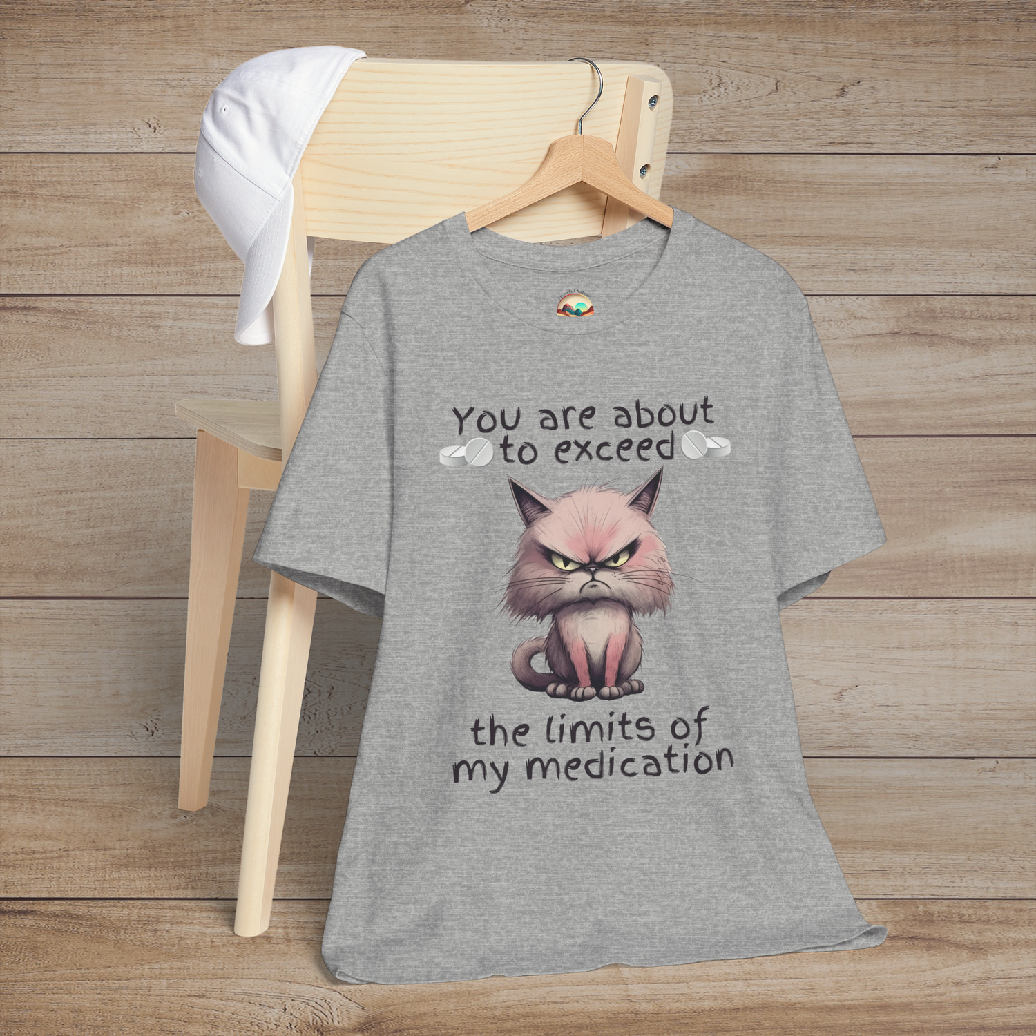 Heather grey funny cranky cat t-shirt featuring angry cartoon cat illustration and sarcastic medication limits quote, laid flat on chair, perfect for cat lovers