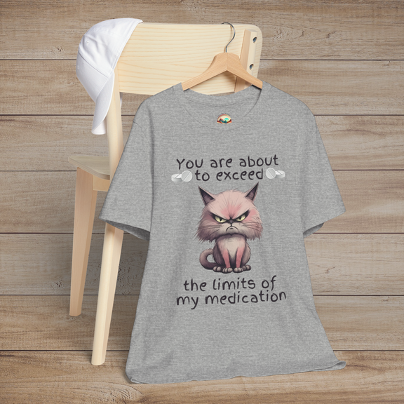 Heather grey funny cranky cat t-shirt featuring angry cartoon cat illustration and sarcastic medication limits quote, laid flat on chair, perfect for cat lovers
