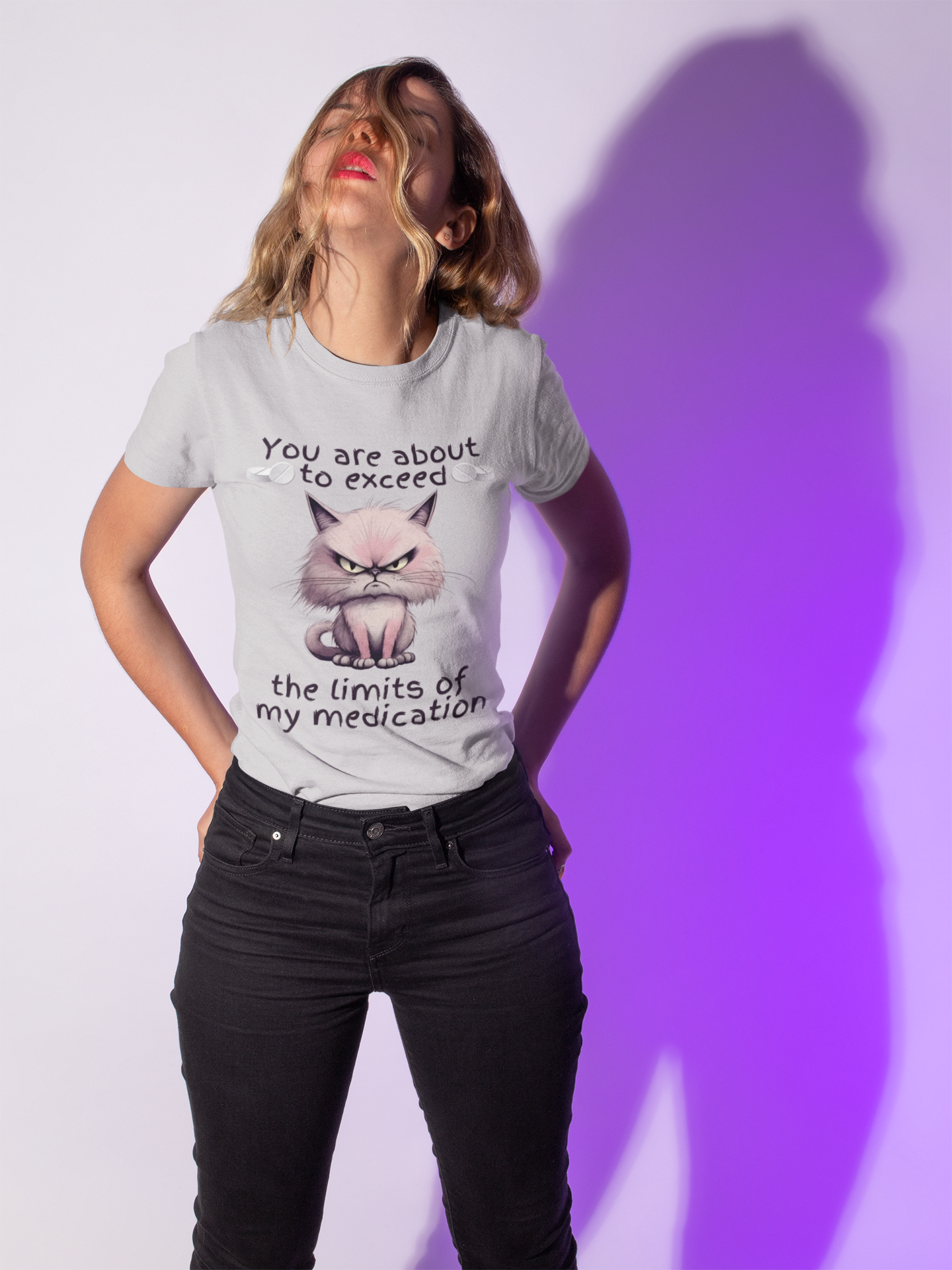 Playful woman wearing heather grey cranky cat t-shirt with angry cartoon cat and funny medication quote, posing under purple lighting, perfect sarcastic gift