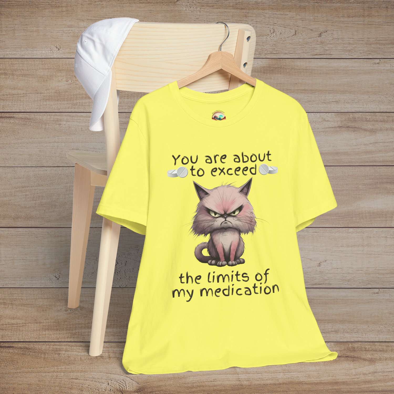 Bright yellow cranky cat t-shirt with angry cartoon cat and sarcastic medication quote, laid flat on chair, perfect humorous gift for cat lovers