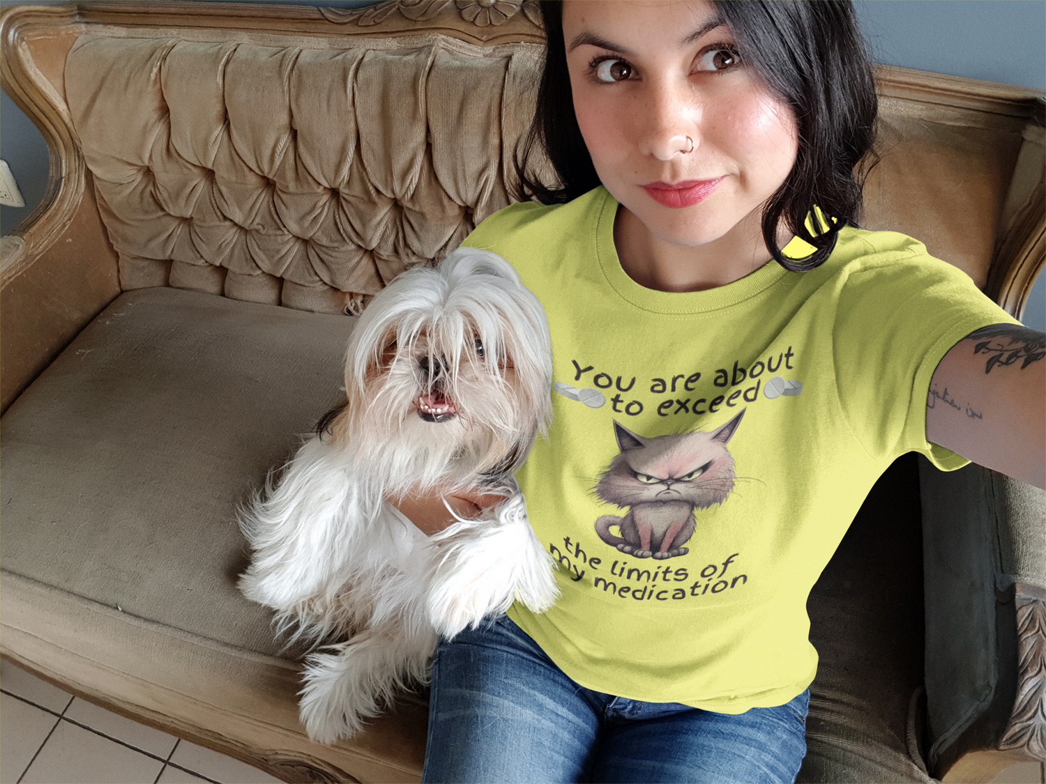 Young woman taking selfie with fluffy dog while wearing yellow funny cranky cat t-shirt with angry cartoon cat graphic and sarcastic quote about patience