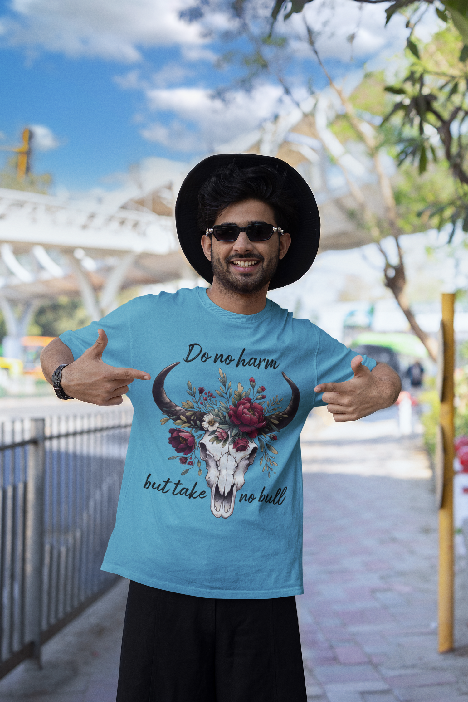 Man wearing a "Do No Harm But Take No Bull" t-shirt in heather aqua, pointing at the design and smiling outdoors