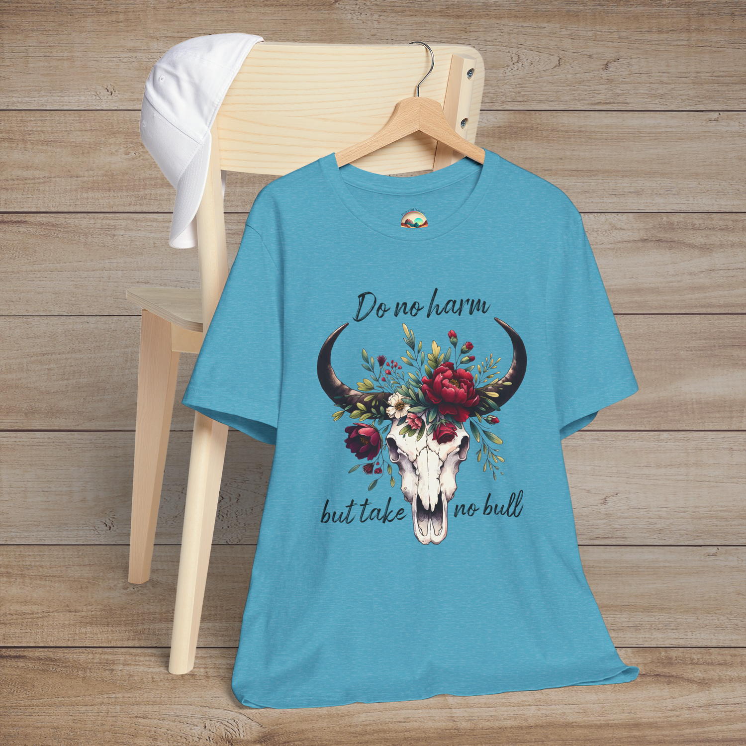 Flat lay of "Do No Harm But Take No Bull" t-shirt in heather aqua with bull skull and floral crown