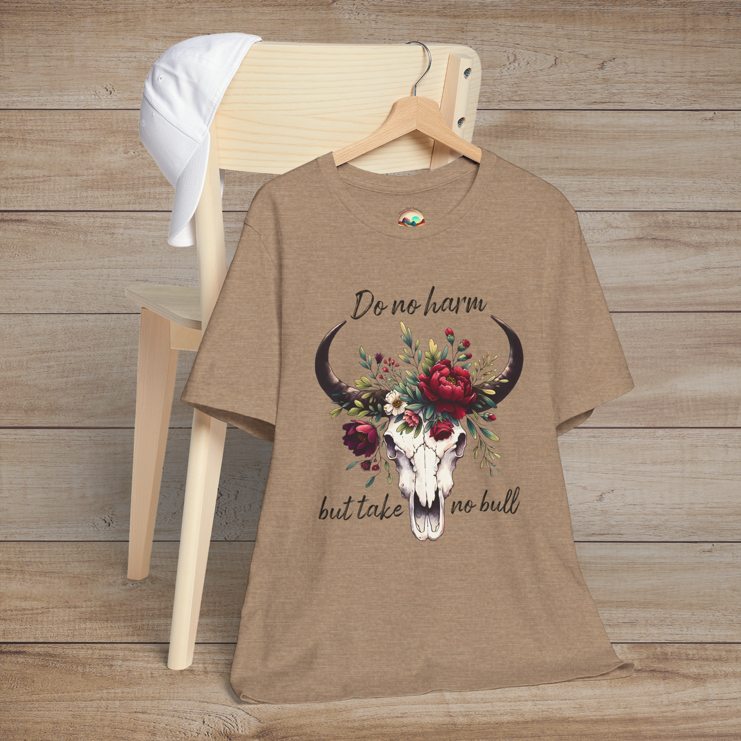 Flat lay of "Do No Harm But Take No Bull" t-shirt in heather tan with bull skull and floral crown
