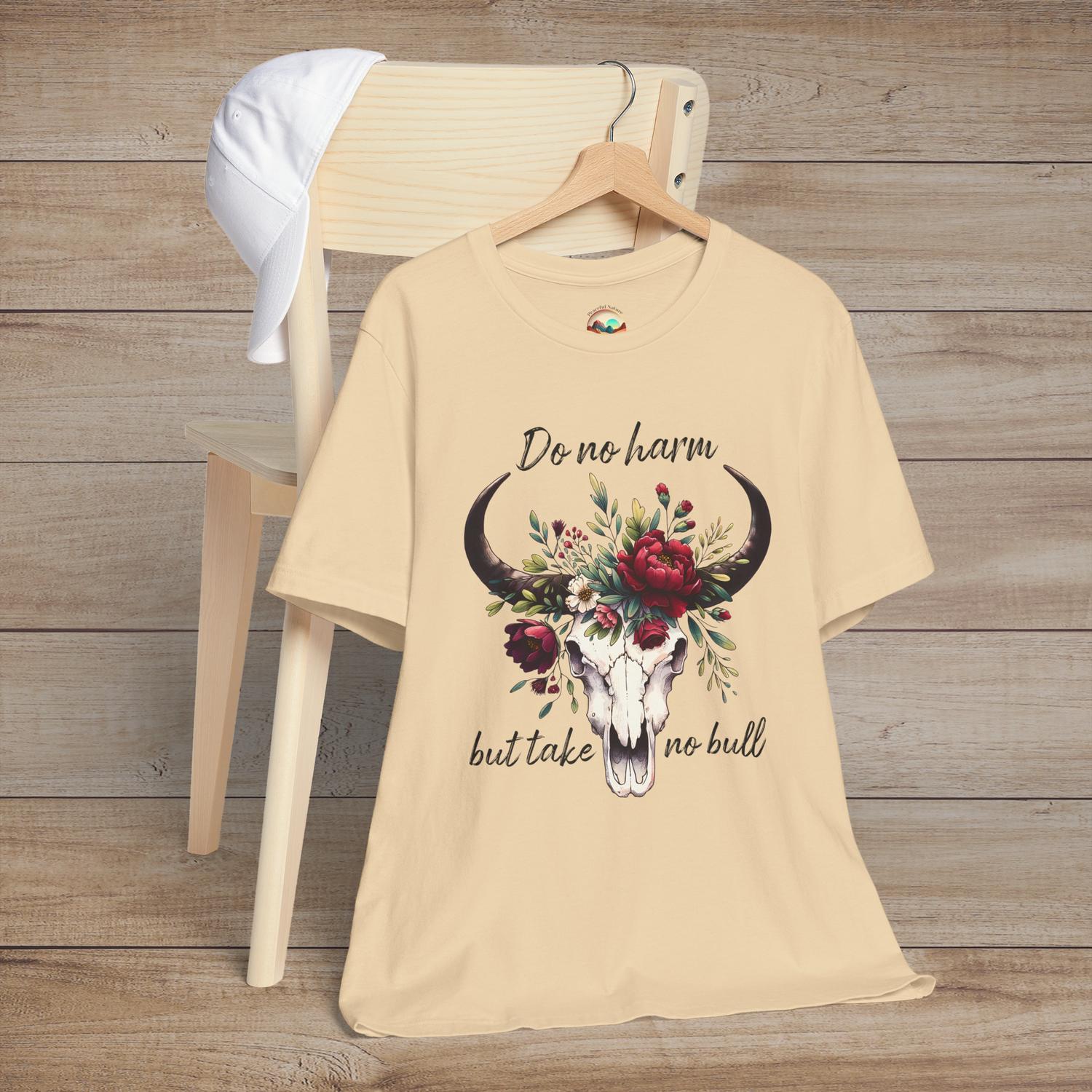 Flat lay of "Do No Harm But Take No Bull" t-shirt in soft cream with bull skull and floral crown