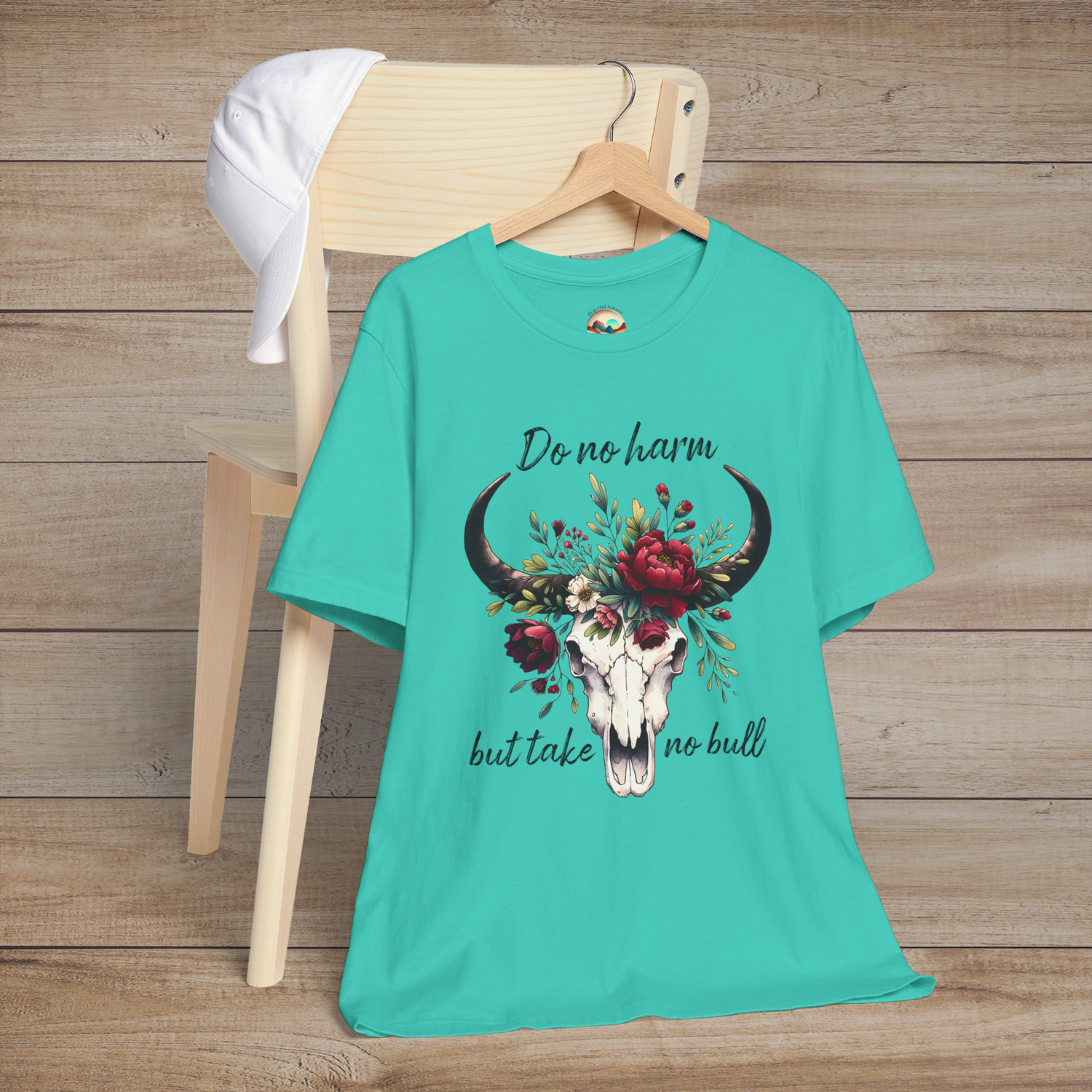 Flat lay of "Do No Harm But Take No Bull" t-shirt in teal with bull skull and floral crown