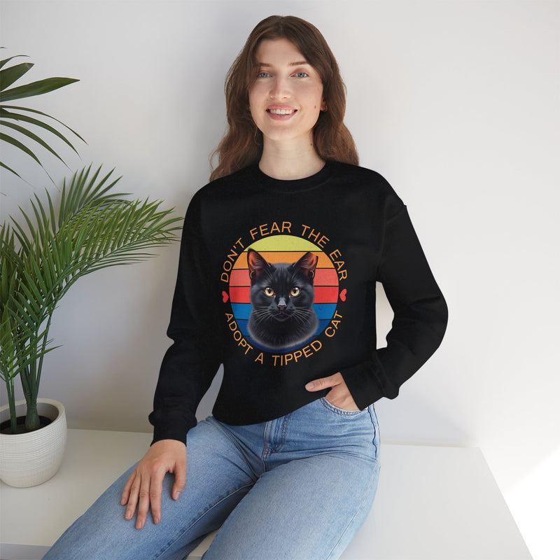 Black Gildan 18000 sweatshirt with ear-tipped black cat artwork and retro sunset circle, worn by smiling woman — ‘Don’t Fear The Ear Adopt a Tipped Cat’ feral cat rescue sweatshirt.