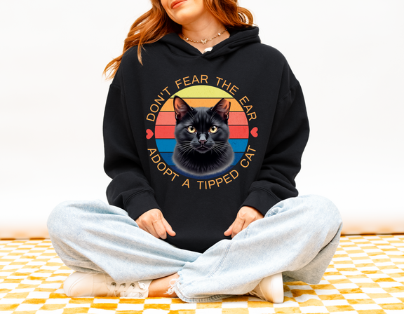 Woman wearing a black “Don’t Fear the Ear – Adopt a Tipped Cat” hoodie featuring a retro black cat design.