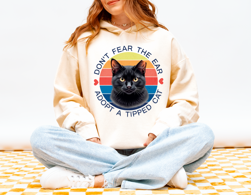 Woman modeling a ivory-colored “Don’t Fear the Ear – Adopt a Tipped Cat” hoodie with a vintage-style black cat graphic.
