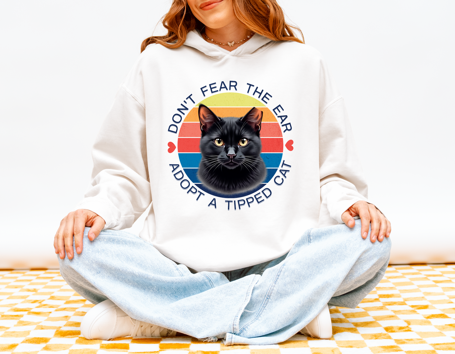 Woman wearing a white “Don’t Fear the Ear – Adopt a Tipped Cat” hoodie with a retro black cat illustration.