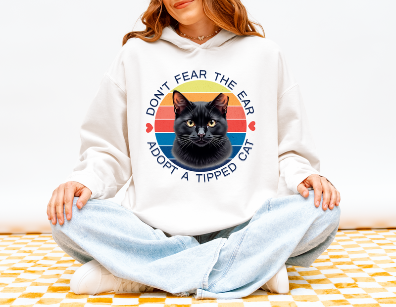 Woman wearing a white “Don’t Fear the Ear – Adopt a Tipped Cat” hoodie with a retro black cat illustration.