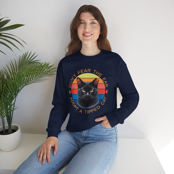 Navy blue Gildan 18000 sweatshirt with ear-tipped black cat design and vintage sunset background, worn by woman indoors — cat adoption and community cat advocate sweatshirt.