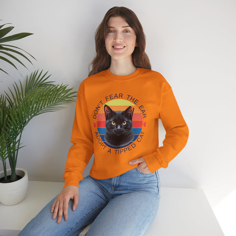 Safety orange Gildan 18000 sweatshirt with ear-tipped black cat design and vintage sunset background, worn by woman indoors — cat adoption and community cat advocate sweatshirt.