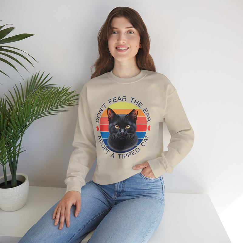 Sand-colored Gildan 18000 sweatshirt with ear-tipped black cat artwork and retro sunset circle, worn by smiling woman — ‘Don’t Fear The Ear Adopt a Tipped Cat’ feral cat rescue sweatshirt.