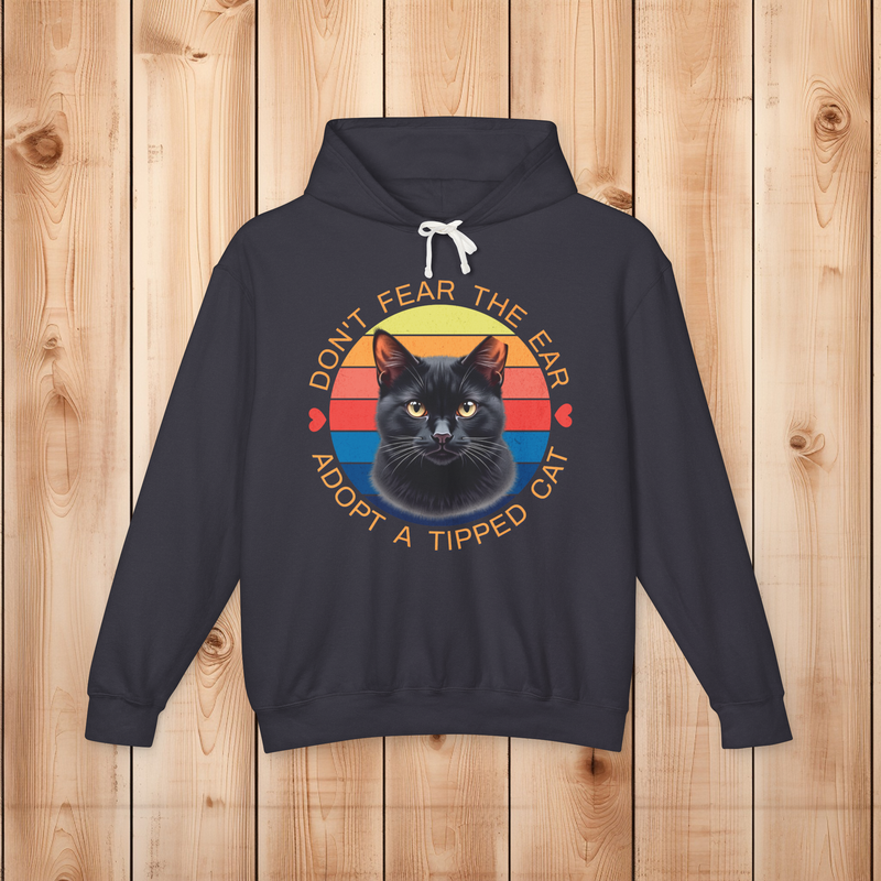 Flatlay of a black “Don’t Fear the Ear – Adopt a Tipped Cat” hoodie with a retro black cat graphic on wood background.