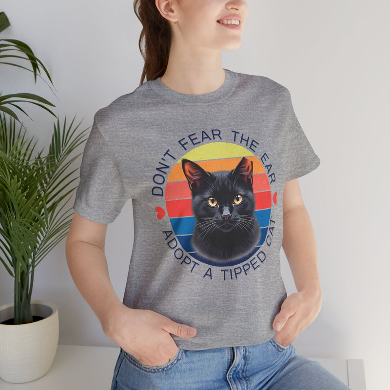Athletic heather Bella Canvas 3001 t-shirt featuring a black cat with an ear tip and retro sunset design, worn by smiling woman indoors — ‘Don’t Fear The Ear Adopt a Tipped Cat’ graphic tee for animal rescue supporters
