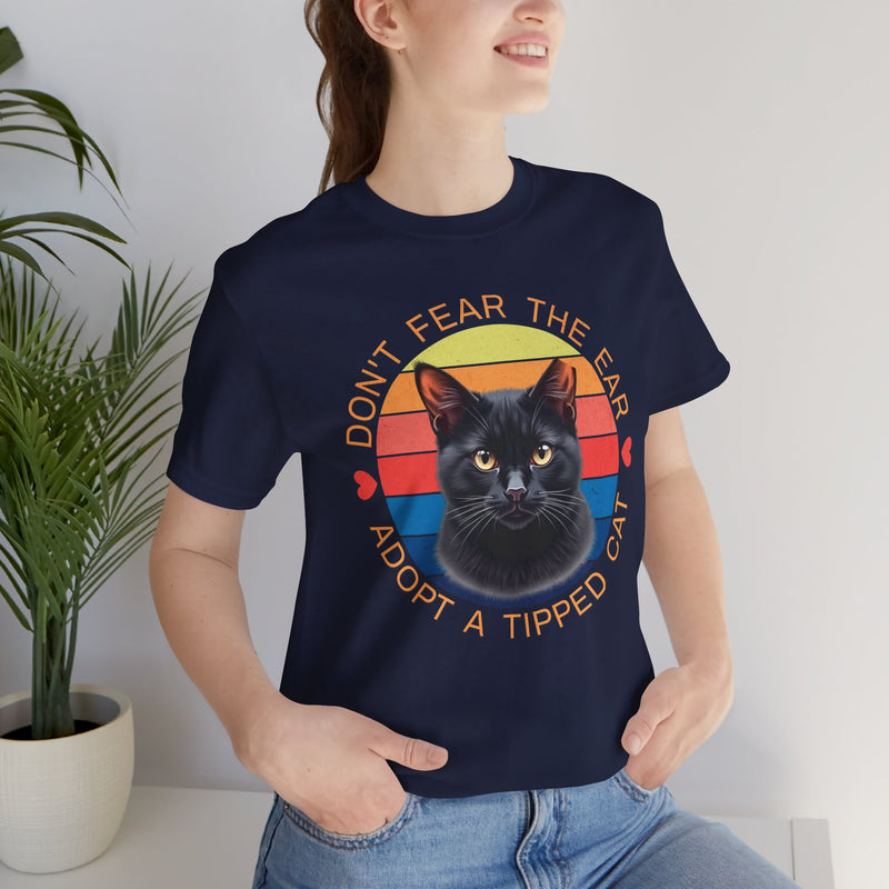 Navy Bella Canvas 3001 t-shirt with ear-tipped black cat design and vintage sunset background, worn by woman indoors — cat adoption and community cat advocate t-shirt