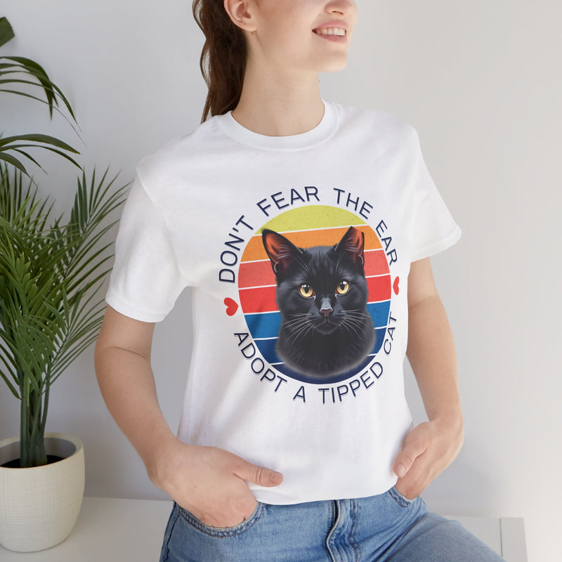 White Bella Canvas 3001 t-shirt displaying ear-tipped black cat graphic and retro rainbow circle, modeled by smiling woman — ‘Adopt a Tipped Cat