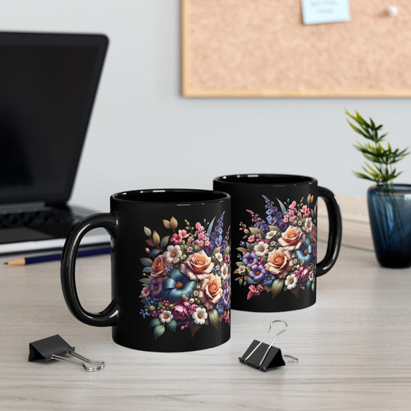 Two 11 oz black ceramic mugs featuring vibrant floral bouquet designs in pinks, reds, blues, and greens, displayed on a wooden desk setup