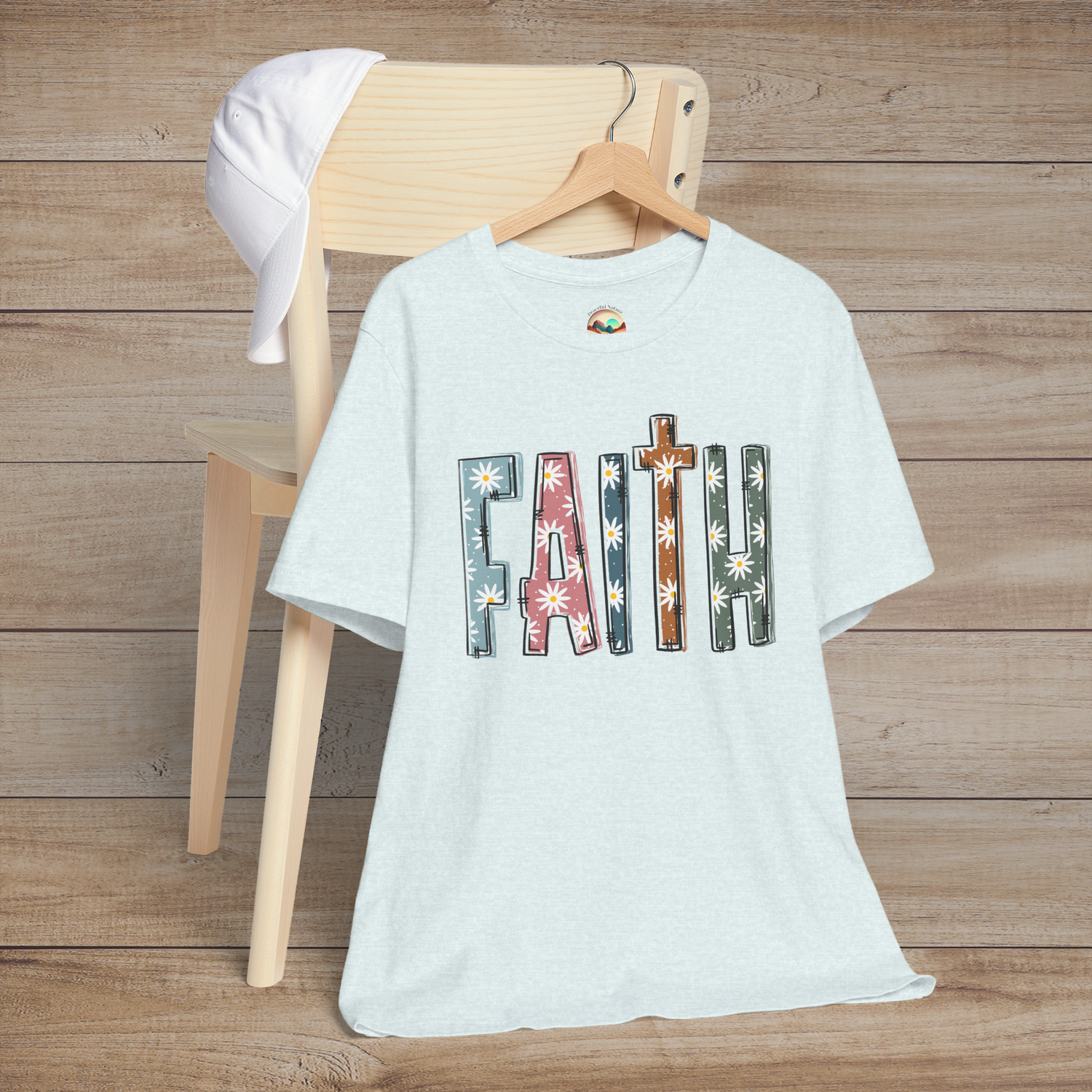 Ice blue premium fit tee with multicolor daisy-filled “FAITH” lettering, hanging neatly on a chair
