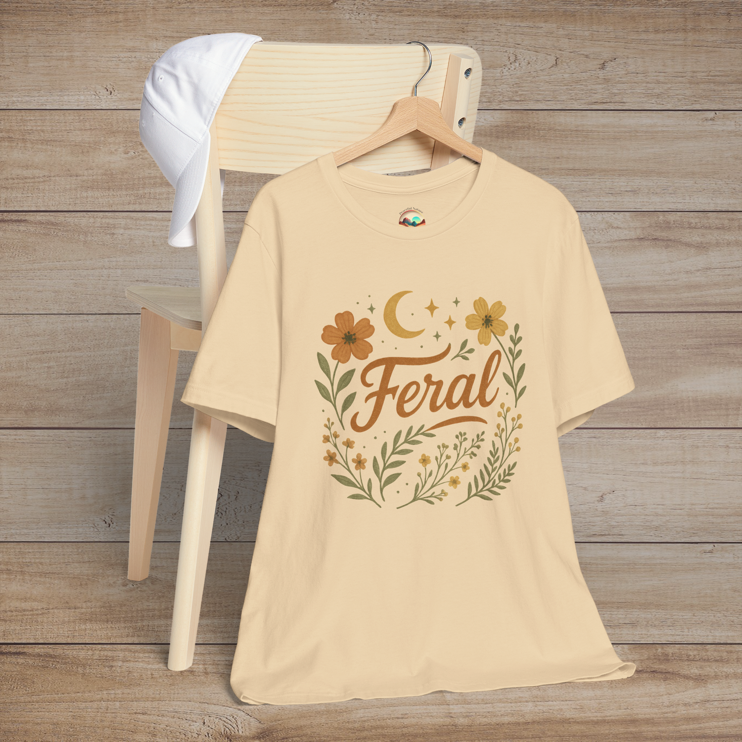 Feral t-shirt in Soft Cream with floral and moon design in elegant calligraphy, displayed on a chair with a cap