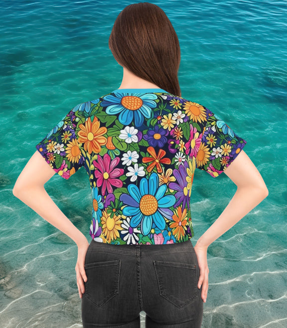 Back view of a woman wearing The Floral Bliss Cropped T-Shirt, featuring a bold and vibrant all-over floral print in red, blue, orange, and yellow hues against a black background with a solid blue neckline