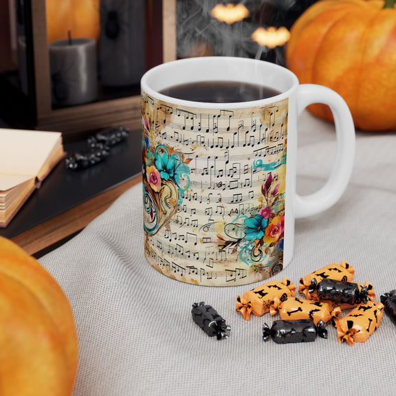 Right-side view of the 11 oz Floral Melody Mug surrounded by Halloween pumpkins and candy, featuring elegant sheet music over vintage parchment with vivid floral accents in teal, orange, and pink. A unique blend of musical and artistic charm