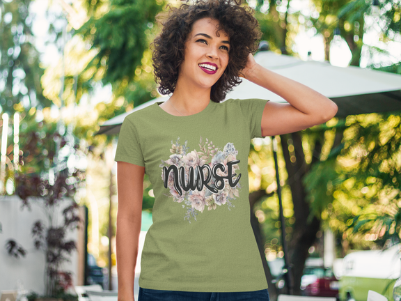 Smiling woman outdoors modeling the heather green Nurse Floral Premium Fit T-Shirt, beautifully designed with soft floral artwork